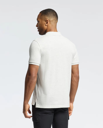 A man with short hair is turned away, highlighting the slim fit MENS JAMES PIQUE POLO - B6K945D200 in light gray by Psycho Bunny, made of durable Pima cotton, paired with black pants against a plain white background.