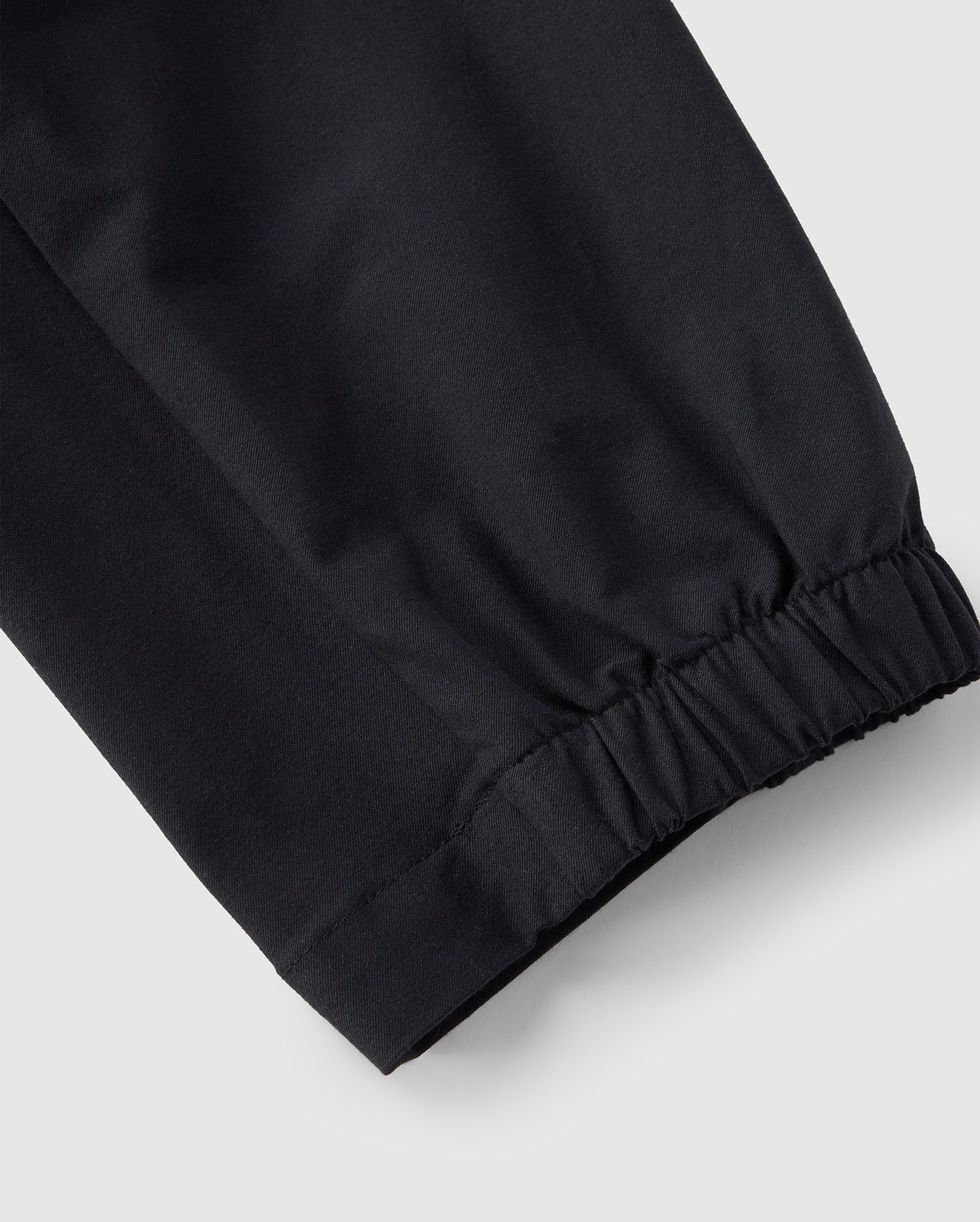 A close-up view of the Psycho Bunny MENS LLOYD CARGO JOGGER - B6P159B200 in black, highlighting the elasticized cuffs. The texture and stitching are clearly visible, showcasing the smooth fabric and gathered design at the end of the jogger legs. The background is plain and light-colored.