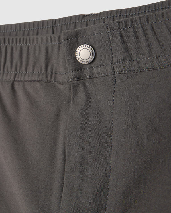 A close-up of the gray MENS MADISON COMMUTER PANT - B6P395Z1WB from Psycho Bunny reveals an elastic waistband and a metal button engraved with "Techwear." The smooth fabric boasts neat stitching and includes a detachable keychain, perfect for the modern commuter.