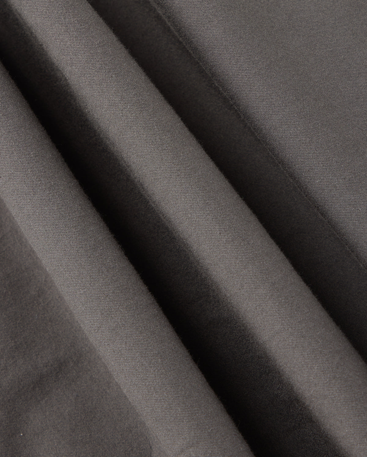 Close-up of dark gray fabric with diagonal folds showcases a soft texture and slight sheen, evoking the sophisticated design characteristic of the Psycho Bunny MENS MADISON COMMUTER PANT - B6P395Z1WB.