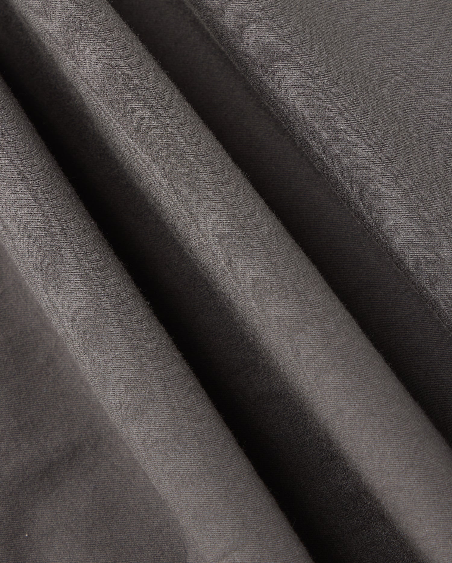 Close-up of dark gray fabric with diagonal folds showcases a soft texture and slight sheen, evoking the sophisticated design characteristic of the Psycho Bunny MENS MADISON COMMUTER PANT - B6P395Z1WB.