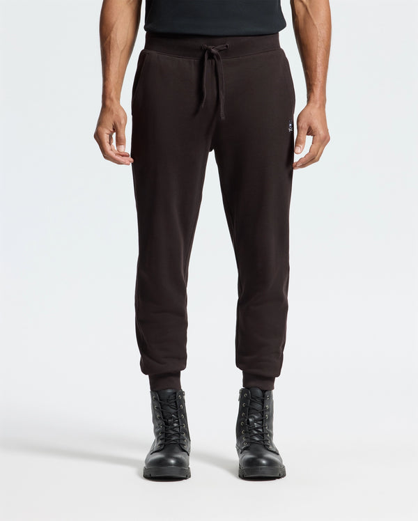 A person in Psycho Bunny's MENS LEVY ESSENTIAL FLEECE SWEATPANT (B6P721D200) and black lace-up boots stands against a white background, exuding a relaxed vibe with their arms at their sides.
