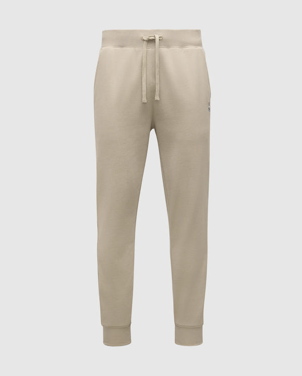 The MENS LEVY ESSENTIAL FLEECE SWEATPANT - B6P721D200 by Psycho Bunny are beige, ultra-soft joggers for men. They feature an elastic waistband with a drawstring, cuffs at the ankles, and a small logo on the left thigh. Made from cozy cotton fabric, these sweatpants are soft and comfortable, making them ideal for casual wear.