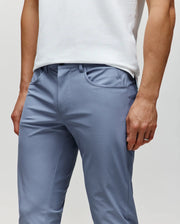 A person wears Psycho Bunny MENS MAVERICK 10K STEP PANT - B6P788D200 in light blue with four-way stretch and a white sleeveless top, right hand by their side, cropped from shoulders to mid-thighs.
