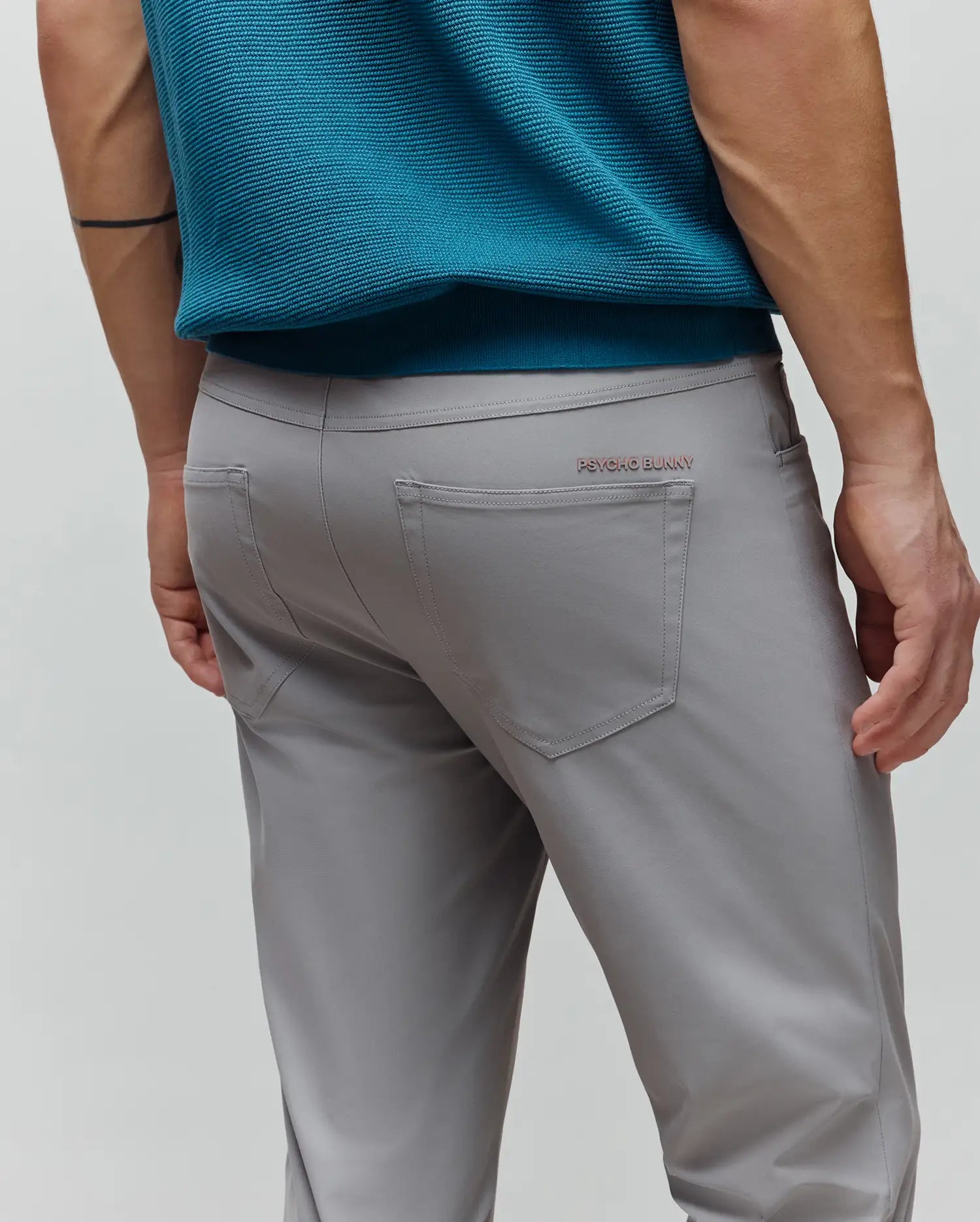 Mens Maverick 10k Step Pant in light grey, featuring a smooth, performance fabric with a classic fit, detailed stitching, and a small rose gold Psycho Bunny text logo above the right back pocket.