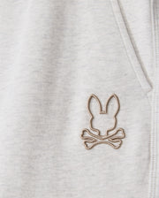 A close-up of the light gray fabric on the Psycho Bunny MENS JAMES PREMIUM SWEATPANT - B6P791D200 highlights a rabbit ears and crossbones logo embroidered near the seam. The logo in light beige offers a distinctive touch to these premium sweatpants, crafted from a soft cotton-blend.