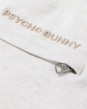 A detailed view of the cotton-blend fabric showcases "Psycho Bunny" elegantly embroidered in beige. Situated below is a small zipper adorned with a bunny icon on the pull tab, injecting a playful element into these MENS JAMES PREMIUM SWEATPANT - B6P791D200, echoing the classic design of James sweatpants by Psycho Bunny.