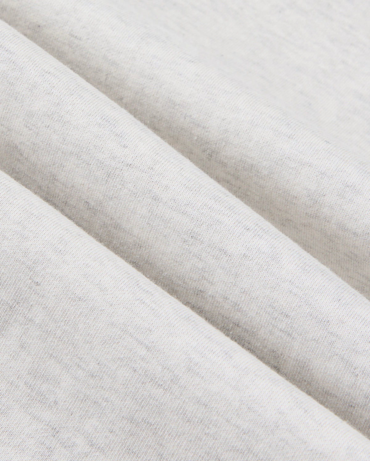 Close-up view of a light gray, cotton-blend fabric with a soft, heathered texture. The fabric is folded in parallel lines, showcasing its smooth and slightly speckled surface—ideal for crafting premium bottoms like the Psycho Bunny MENS JAMES PREMIUM SWEATPANT - B6P791D200.