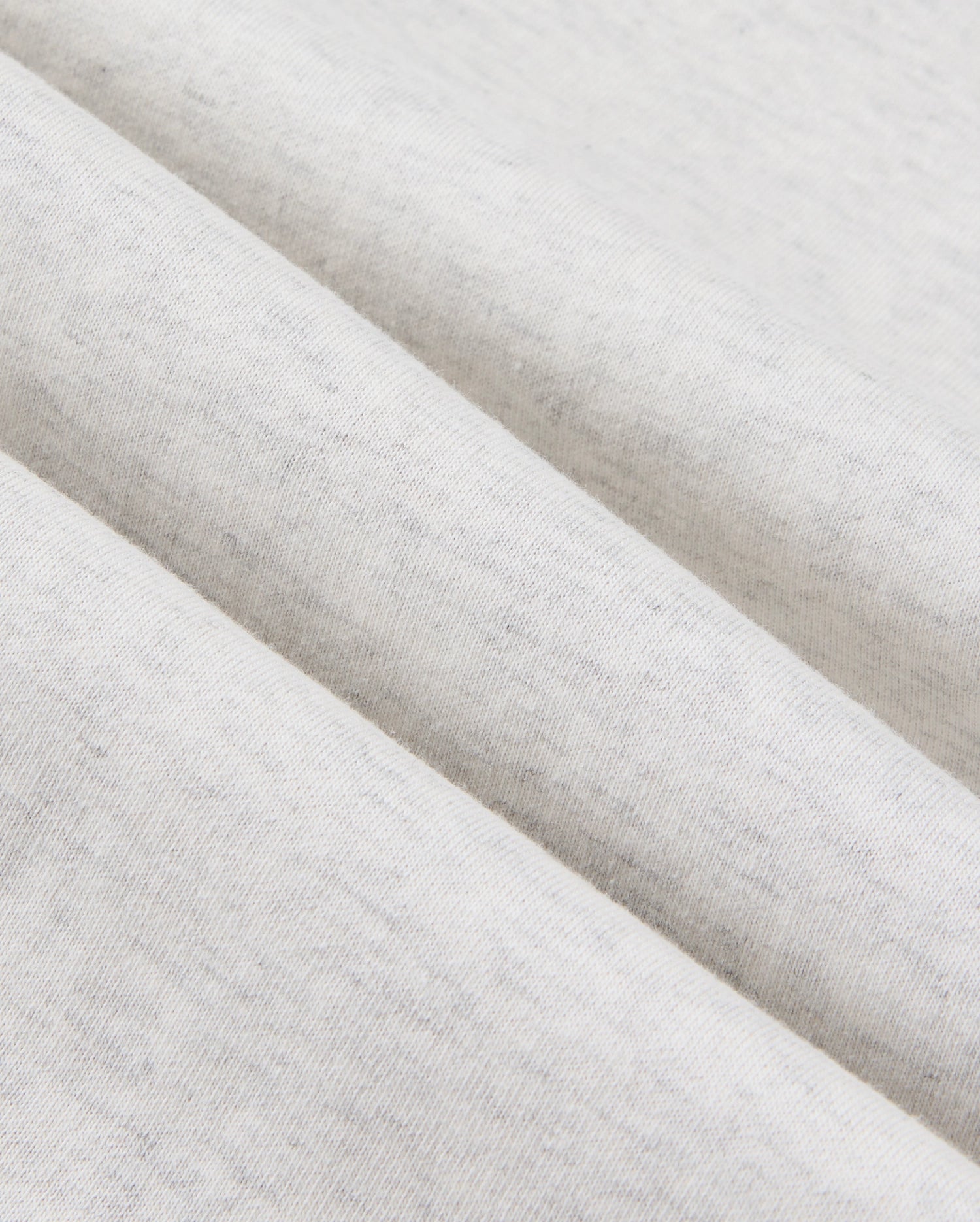 Close-up view of a light gray, cotton-blend fabric with a soft, heathered texture. The fabric is folded in parallel lines, showcasing its smooth and slightly speckled surface—ideal for crafting premium bottoms like the Psycho Bunny MENS JAMES PREMIUM SWEATPANT - B6P791D200.
