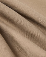 Close-up of the Psycho Bunny MENS HAYS TWILL PANT - B6P894D200, made from a soft beige cotton-blend twill with a textured surface featuring diagonal ridges. The four-way stretch material drapes in gentle folds, creating subtle shadows and highlights.