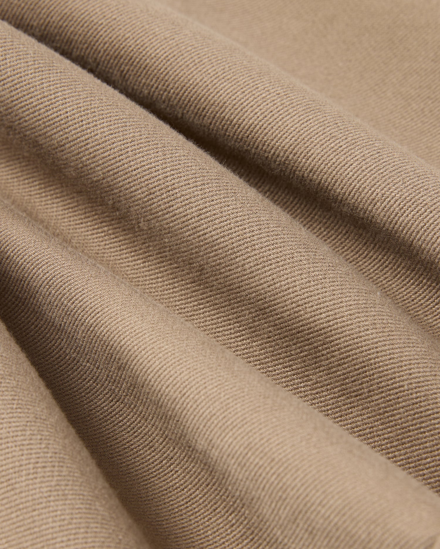 Close-up of the Psycho Bunny MENS HAYS TWILL PANT - B6P894D200, made from a soft beige cotton-blend twill with a textured surface featuring diagonal ridges. The four-way stretch material drapes in gentle folds, creating subtle shadows and highlights.