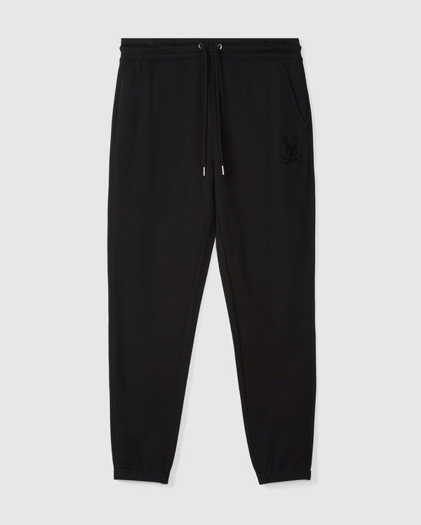 The Psycho Bunny Men's Pacific Chenille Jogger - B6P972D200 showcases a casual bottom design with black jogger pants and a drawstring waistband. Its style is enhanced by side pockets and ribbed cuffs, along with a high-pile chenille logo patch featuring a rabbit head embroidered on the upper left side, all set against a plain white background.