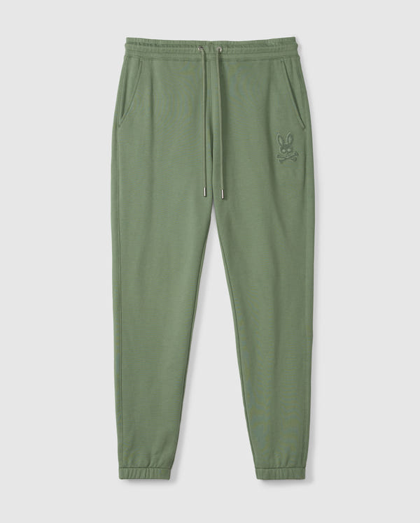 The Psycho Bunny MENS PACIFIC CHENILLE JOGGER - B6P972D200 in olive green comes with an elastic waistband and adjustable drawstring. These casual bottoms are equipped with side pockets, a prominent high-pile chenille logo patch on the left thigh, and ribbed cuffs for a snug fit, all presented against a plain background.