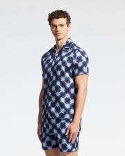 A person wearing the Psycho Bunny MENS PAROS TENCEL SHIRT in a blue and white wavy pattern stands against a plain white background, paired with matching shorts.