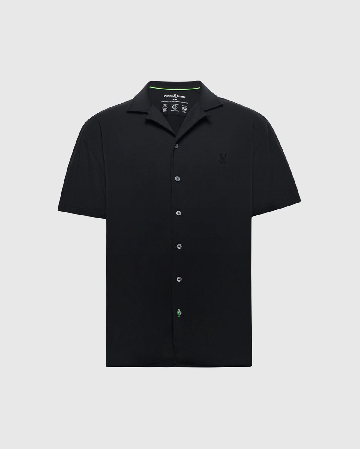 The Psycho Bunny MENS BRYAN CAMP COLLAR SHORT SLEEVE SHIRT - B6Q581F200 is a black Pima cotton shirt with a camp collar and subtle left chest embroidery. It features a minimalistic design with a discreet green logo near the bottom button.