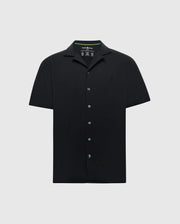 The Psycho Bunny MENS BRYAN CAMP COLLAR SHORT SLEEVE SHIRT - B6Q581F200 is a black Pima cotton shirt with a camp collar and subtle left chest embroidery. It features a minimalistic design with a discreet green logo near the bottom button.