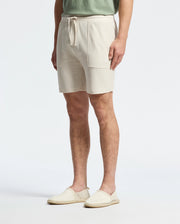 Sporting a casual-chic vibe in Psycho Bunny's MENS TAYLOR LIGHT PIQUE SWEATSHORT (B6R344F200), featuring pockets and a drawstring, paired with a lightweight light green shirt and beige espadrilles, they effortlessly stand against a plain white backdrop.