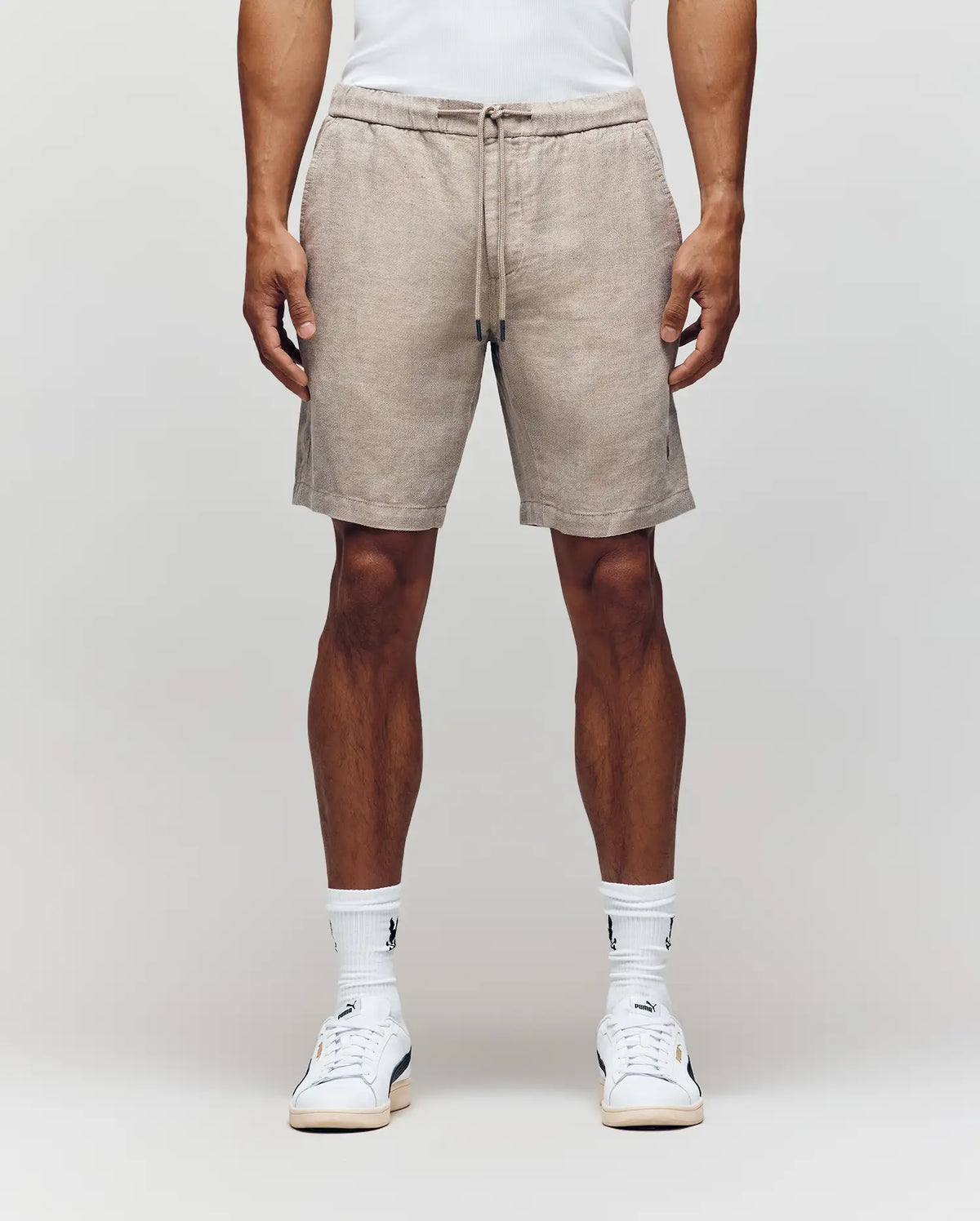 Wearing Psycho Bunny’s MENS WINDCREST LINEN BLEND DRAWSTRING SHORT (B6R474C200), a white tank top, crew socks, and white sneakers, a person stands against a plain light background. Image is cropped from shoulders to feet.