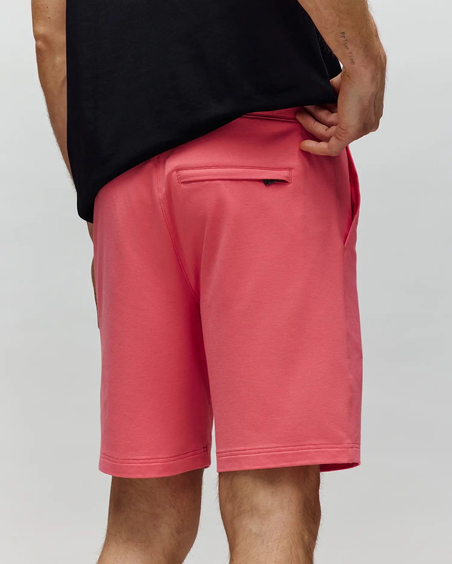 A person is shown from the waist down wearing Psycho Bunny's MENS LEVANZO FRENCH TERRY SWEATSHORT - B6R578F200 in bright pink. Made from micro French terry, the shorts feature a zippered back pocket. The background is light gray.