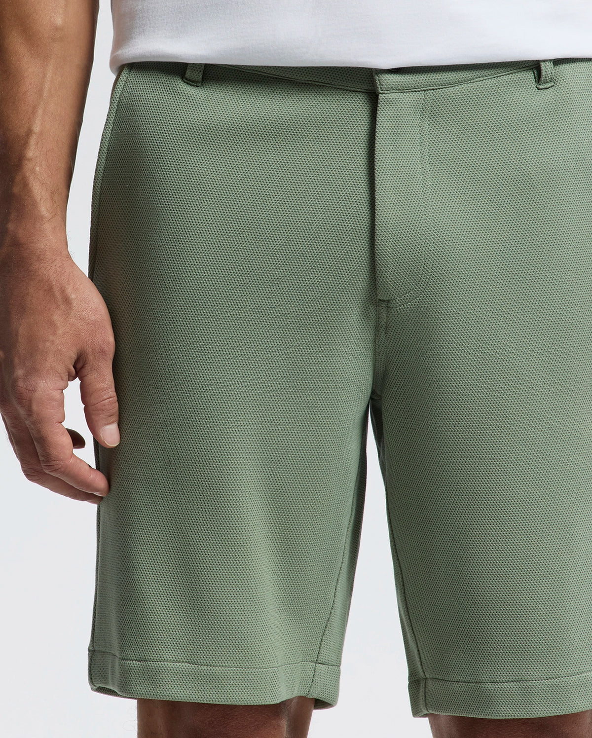 Wearing Psycho Bunny's light green MENS SHIRO KNIT HONEYCOMB SHORT with a honeycomb piqué and belt loops, paired with a white shirt, only part of the person's torso and right hand are visible against a light background, highlighting the stylish versatility of this B6R585F200 piece.