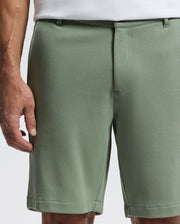 Wearing Psycho Bunny's light green MENS SHIRO KNIT HONEYCOMB SHORT with a honeycomb piqué and belt loops, paired with a white shirt, only part of the person's torso and right hand are visible against a light background, highlighting the stylish versatility of this B6R585F200 piece.