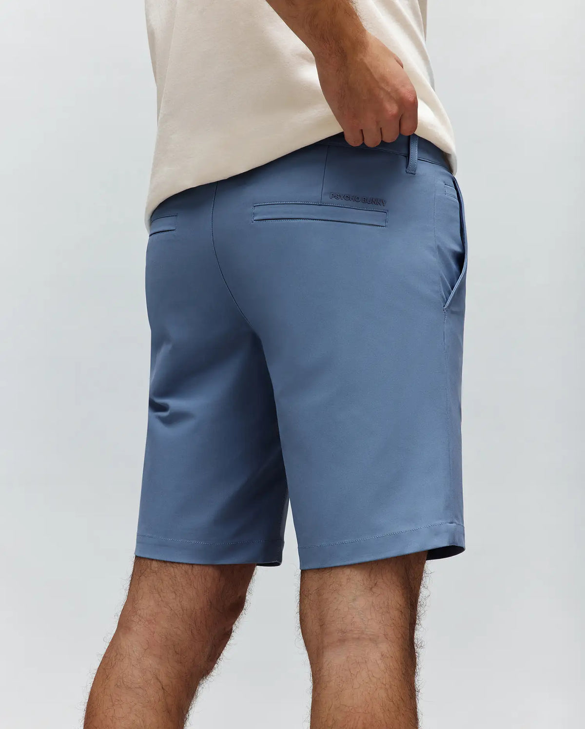 Mens Maverick 10k Step Short in dusty blue, featuring a classic fit, smooth performance fabric, rear welt pockets, and a small tonal embroidered Psycho Bunny wordmark above the right back pocket.