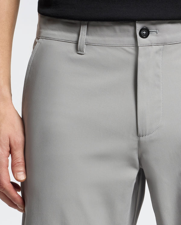 Close-up of someone in light gray Psycho Bunny MENS 10K STEP SHORT - B6R969F200 with breathable fabric, a side pocket, and a single button waistband, paired with a black top. A hand rests nearby, accentuating athletic elegance.