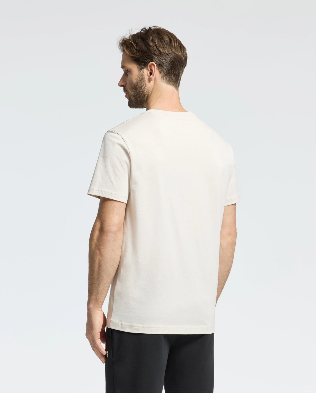 A man with brown hair, facing away from the camera against a plain background, wears a Psycho Bunny MENS CLASSIC CREW NECK TEE - B6U014B200 in vibrant colors, paired with black pants.