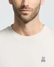 A man dons a Psycho Bunny MENS CLASSIC CREW NECK TEE - B6U014B200, crafted from premium Pima cotton with a small embroidered pink bunny and crossed bones logo on the chest. His subtle expression and facial hair complement the tee's vibrant colors.