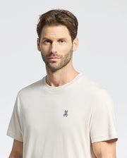 A man with short brown hair and a beard wears the Psycho Bunny MENS CLASSIC CREW NECK TEE - B6U014B200, made from premium Pima cotton with a small embroidered rabbit logo on the chest, standing against a plain light gray background.