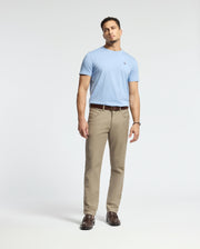 A man stands against a plain background, wearing a light blue Psycho Bunny MENS CLASSIC CREW NECK TEE (B6U014B200), beige pants, and brown loafers. He has short hair and relaxed hands by his sides. The outfit is casual, coordinated, and subtly embraces vibrant colors.