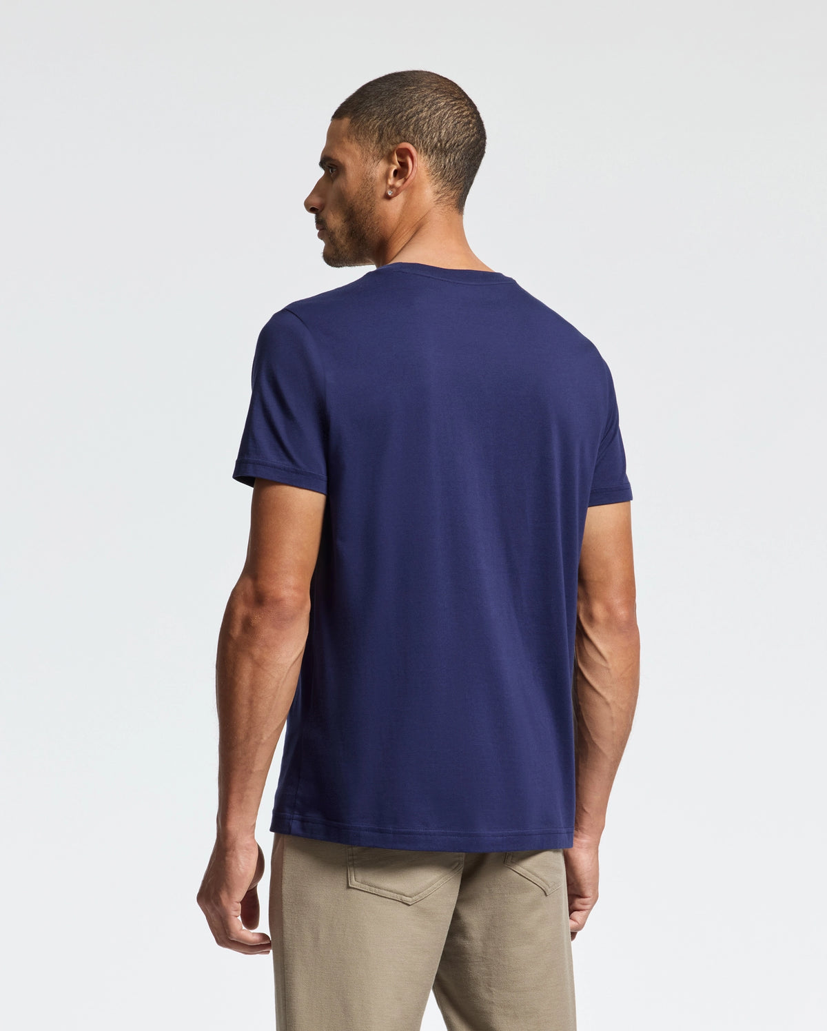A man wearing the Psycho Bunny MENS CLASSIC CREW NECK TEE - B6U014CRPC in navy blue and beige pants stands against a plain white background, viewed from behind.