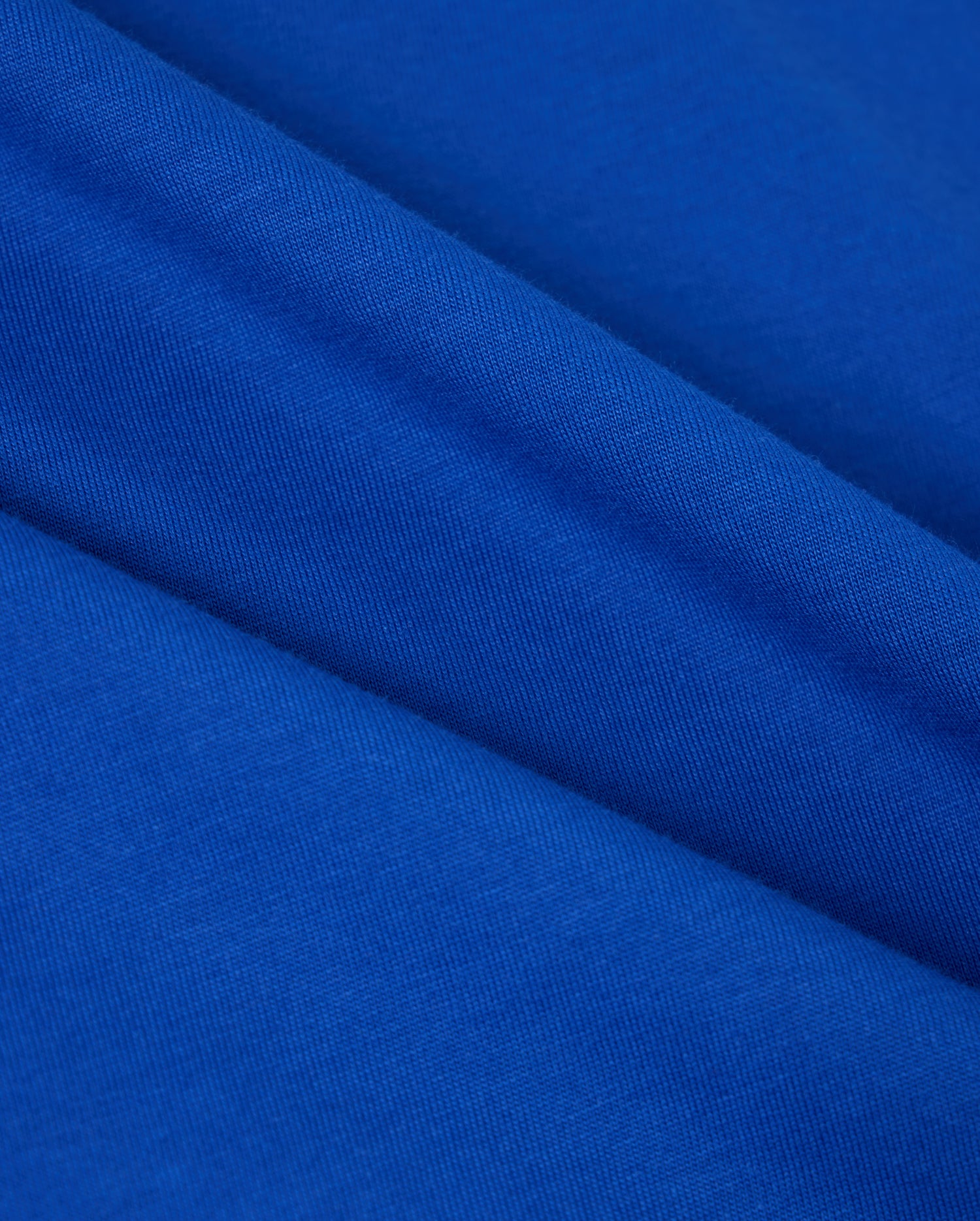 A close-up of the Pima cotton fabric from the Psycho Bunny MENS CLASSIC CREW NECK TEE - B6U014CRPC reveals its smooth texture and diagonal folds. The fabric looks soft and uniform, exhibiting a rich, consistent blue hue throughout—ideal for creating a cozy crewneck tee.