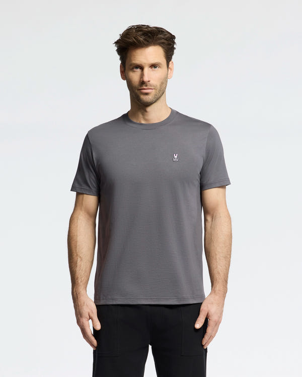A man in a versatile Psycho Bunny MENS CLASSIC CREW NECK TEE (B6U014F200) with a small logo on the left chest stands against a white background; his short brown hair complements the casual style of this classic pima cotton tee.