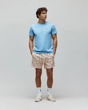 Light blue Mens Classic Crew Neck Tee, classic fit jersey, with small embroidered Psycho Bunny skull logo. Paired with cream relaxed fit shorts, vibrant multi-color grid pattern, and integrated bunny skull logos.