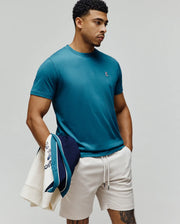 Mens Classic Crew Neck Tee in rich teal, featuring a classic fit and smooth jersey knit. A small, embroidered Psycho Bunny skull logo with pink, white, and black accents is on the left chest.