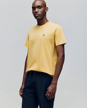 A man stands against a light gray background wearing the Psycho Bunny MENS CLASSIC CREW NECK TEE - B6U014F200 in vibrant yellow with a small chest graphic, paired with black pants.