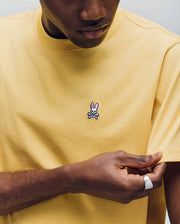A man in a Psycho Bunny MENS CLASSIC CREW NECK TEE (B6U014F200), featuring a small pink-eared bunny skull and crossbones logo on the chest, holds the sleeve gently with one hand.