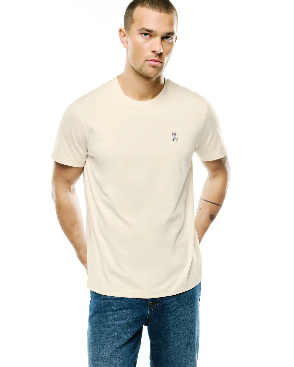 Mens Classic Crew Neck Tee in cream, featuring a small embroidered Psycho Bunny skull logo in pink, purple, black, and white on the left chest, with a classic fit and smooth jersey knit. (1)