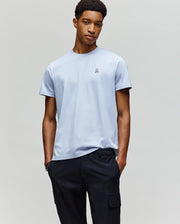 A young man stands with his hands in his pockets, wearing a Psycho Bunny MENS CLASSIC CREW NECK TEE - B6U014F200 in light blue and black pants, set against a plain light gray background.