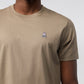 Close-up of a man wearing a beige, 100% Pima cotton MENS CLASSIC CREW NECK TEE featuring a small, white Psycho Bunny embroidered logo on the left chest. Only the torso is visible.