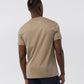 Rear view of a man wearing a beige, 100% Pima cotton MENS CLASSIC CREW NECK TEE - B6U014CRPC from Psycho Bunny and blue jeans. The man has a stylish braided hairstyle.