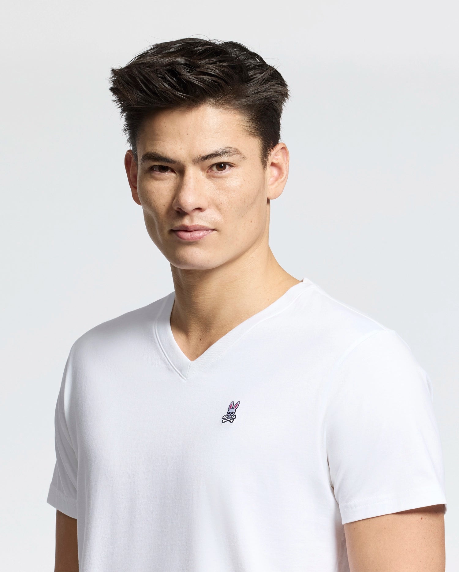 A person with short hair wears a Psycho Bunny Men's Classic V-neck Tee (B6U100ARPC) made from 100% Pima cotton, featuring a small embroidered logo on the chest, set against a plain white background.
