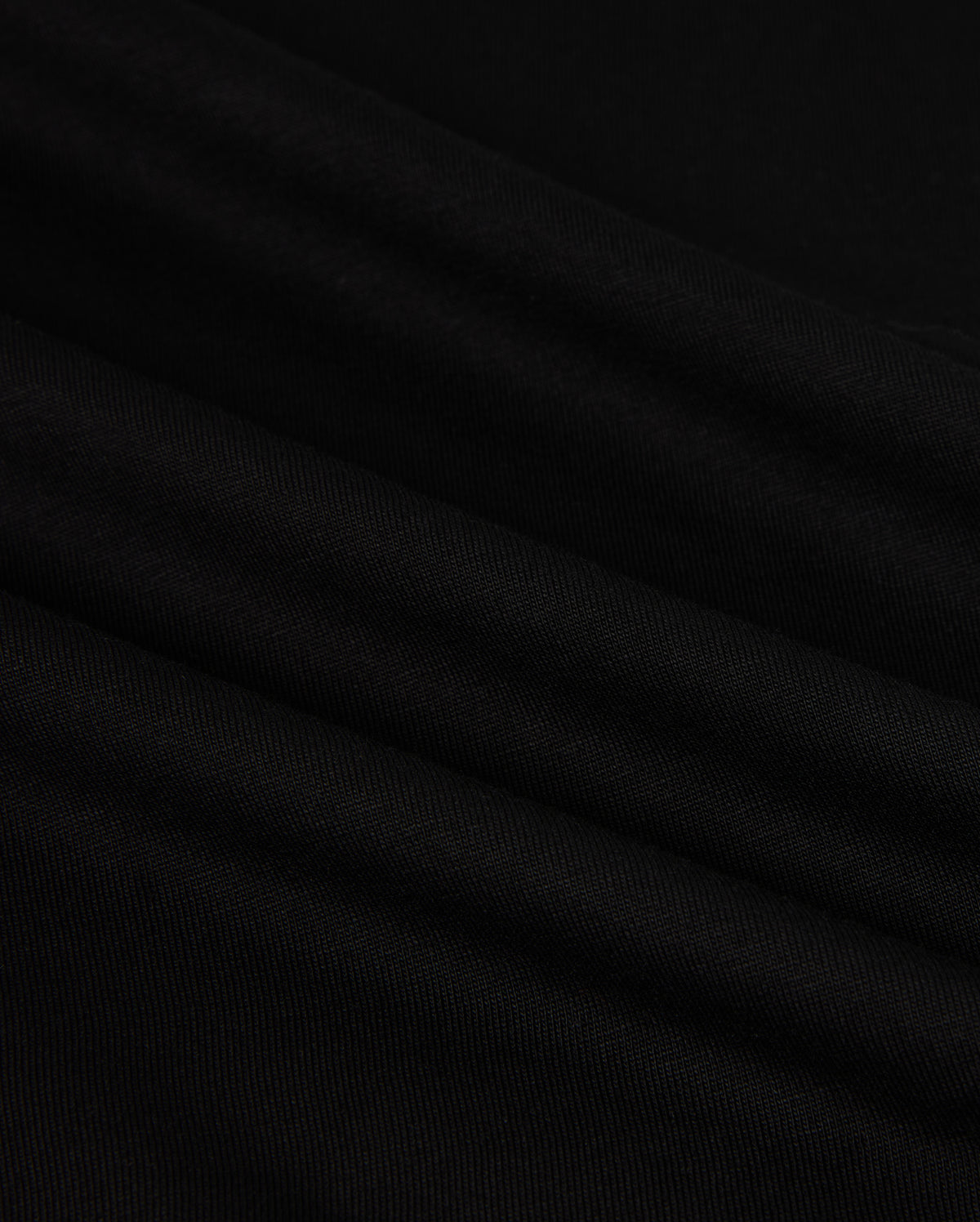 Close-up of the MENS HAWAII CITY TEE - B6U169Y1PC by Psycho Bunny, made from black Pima cotton fabric with a smooth, slightly rippled texture. The dark material displays gentle folds and a subtle sheen, resembling the luxurious quality of a sophisticated men's T-shirt for an elegant appearance.