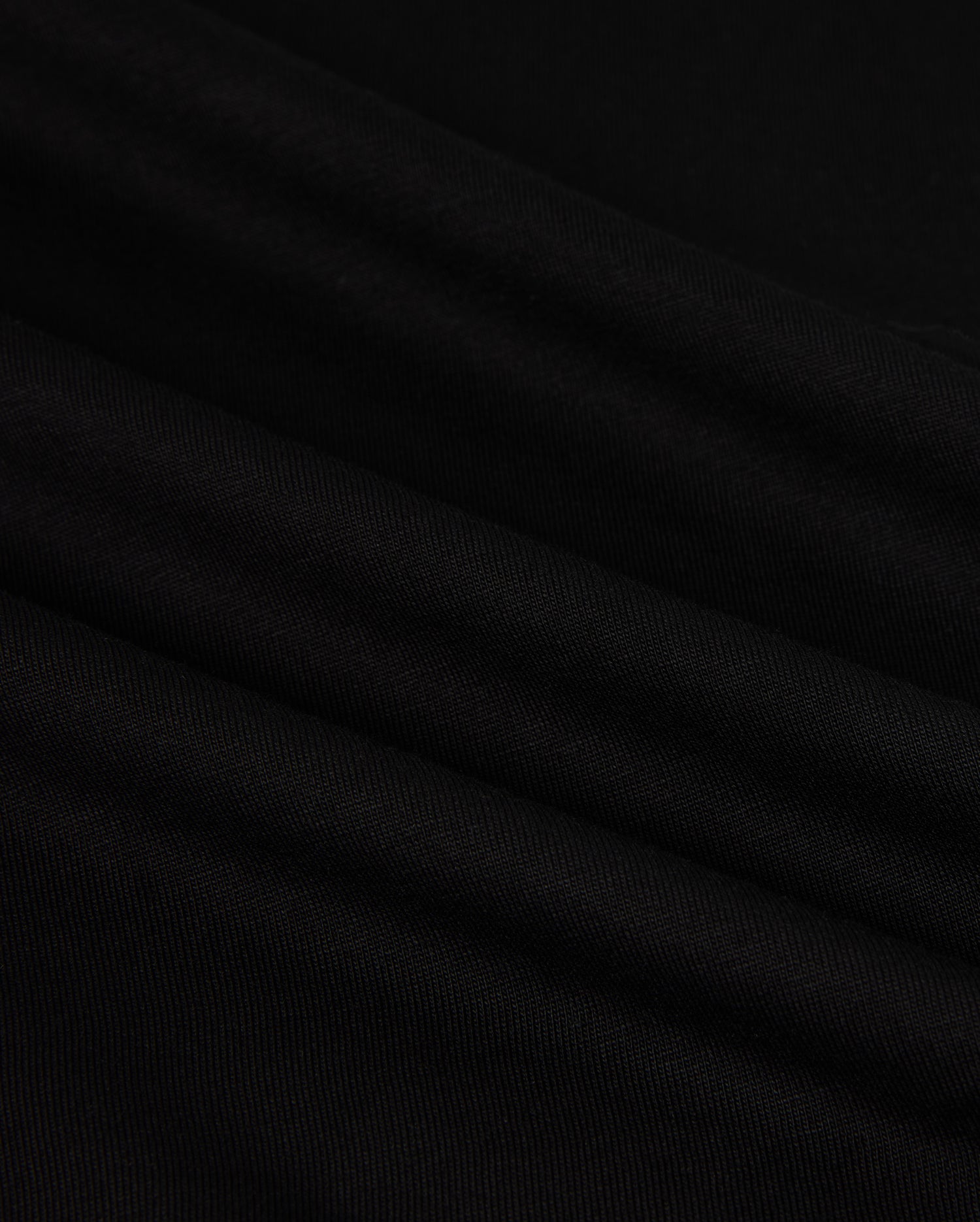 Close-up of the MENS HAWAII CITY TEE - B6U169Y1PC by Psycho Bunny, made from black Pima cotton fabric with a smooth, slightly rippled texture. The dark material displays gentle folds and a subtle sheen, resembling the luxurious quality of a sophisticated men's T-shirt for an elegant appearance.