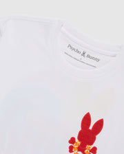 Close-up of a white Psycho Bunny MENS HAWAII CITY TEE - B6U169Y1PC crafted from soft Pima cotton jersey. The shirt features a red bunny graphic pattern with textured details and a small floral design in yellow and red near the bottom right. The neckline label displays the brand's name and logo.