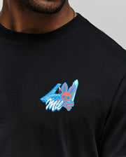 Close-up of a person wearing the Psycho Bunny MENS MONTREAL TEE (B6U381F200), a soft black Pima cotton shirt with a chest graphic featuring a pink bunny with crossbones, blue crystals, and "Mil"—a tribute to Montreal style.