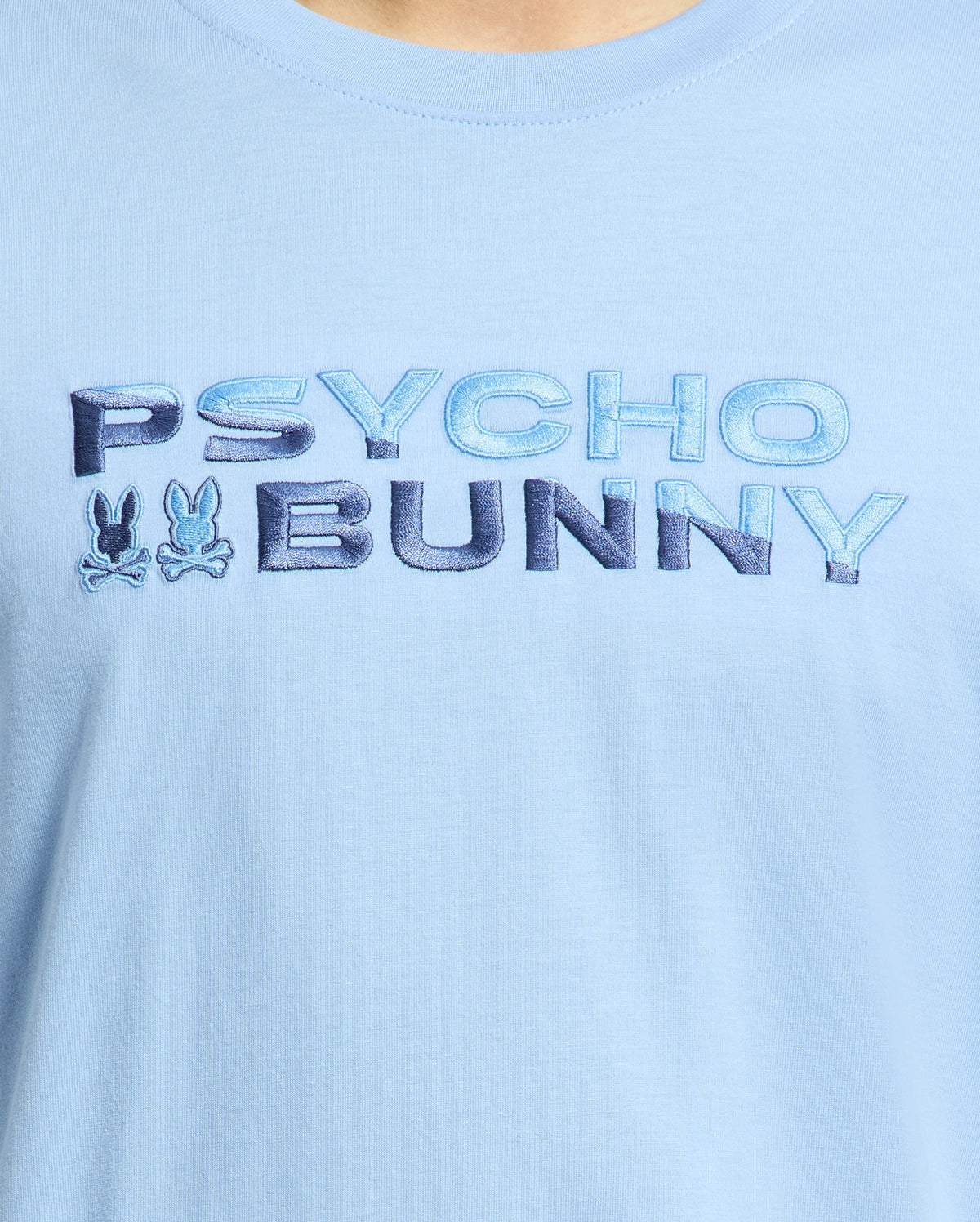 The Psycho Bunny MENS BERNI EMBROIDERED WORDMARK GRAPHIC TEE - B6U417F200 is a light blue premium Pima cotton shirt, featuring "Psycho Bunny" in gradient blue letters with two bunny silhouettes and crossed bones beneath. It's exceptionally crafted and made in Peru.
