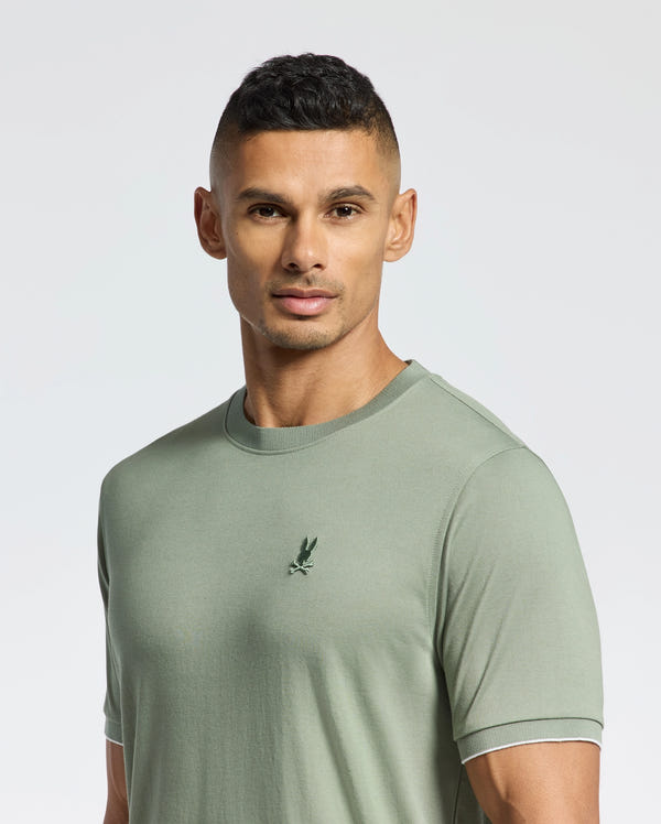 A man wears a light green Psycho Bunny MENS BRYCE PERFORMANCE TEE (B6U490F200) with a small bird logo on the left chest, made of soft Pima cotton, against a plain white background.