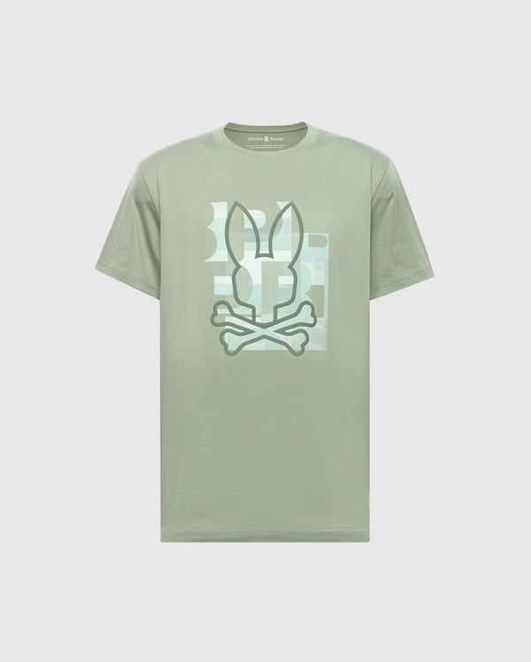 The Psycho Bunny MENS ZEALAND GRAPHIC TEE (B6U604F200) is a light green shirt with a stylized bunny ears and crossed bones graphic on the chest, framed by a subtle rectangular background pattern.
